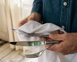 دستی که قاشق و چنگال استیل را با دستمال تمیز خشک می‌کند، نمادی از ضدعفونی و بهداشت آشپزخانه.